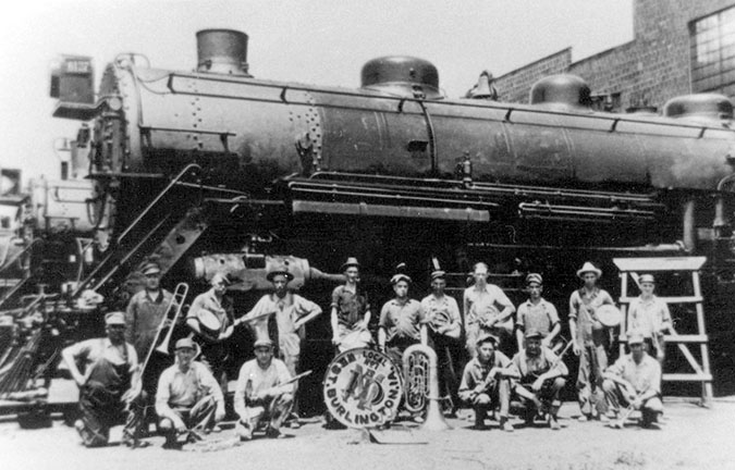 Taken after a weekly rehearsal, the West Burlington Shop Band poses beside a steam locomotive in the late 1920s.